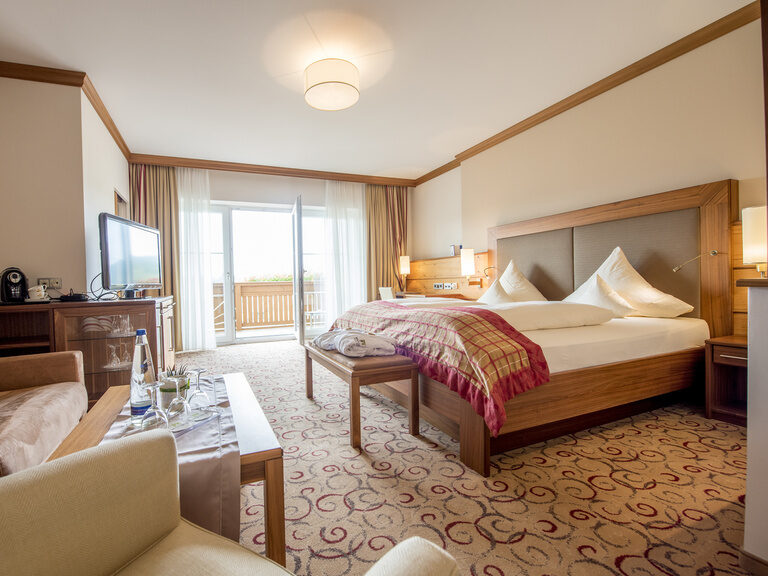 Bequeme Sitzgelegenheiten und ein großzügiges Bett in der Gartensuite Schwalbennest des Wellnesshotels Mooshof in Bayern.