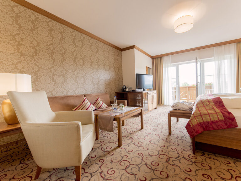 Komfortable hell beleuchtete Sitzecke mit Flachbildfernseher in der Gartensuite Schwalbennest des Wellnesshotels Mooshof im Bayerischen Wald.