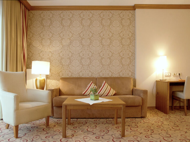 Der Wohnbereich der Gartensuite des Wellnesshotels Mooshof in Bayern bietet komfortable Sitzgelegenheiten und einen Arbeitsplatz mit Schreibtisch.