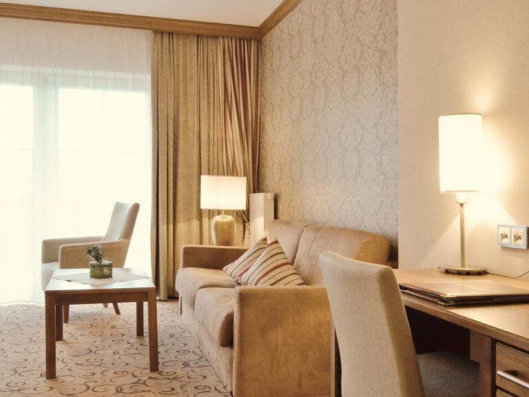 Gemütliche Couch mit designorientierter Beleuchtung und praktischen Schreibtisch in der Gartensuite des Wellnesshotels Mooshof im Bayerischen Wald.