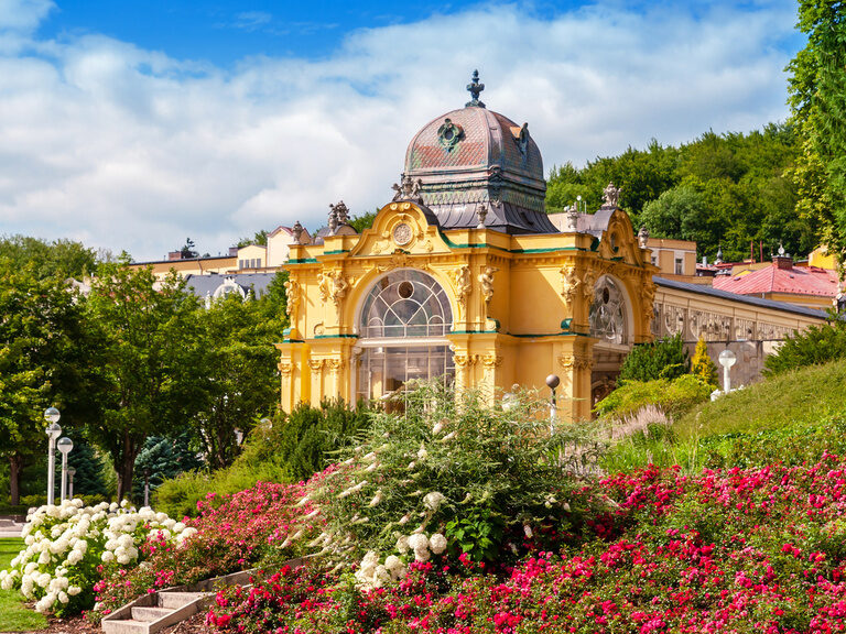 Ein gelbes Schloss umgeben von einem idyllischen Garten mit Blumen und Büschen.