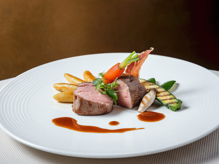 Ein köstliches Ensemble des Restaurants im Hotel Mooshof aus zartem Fleisch und knackigem Gemüse auf einem weißen Teller.