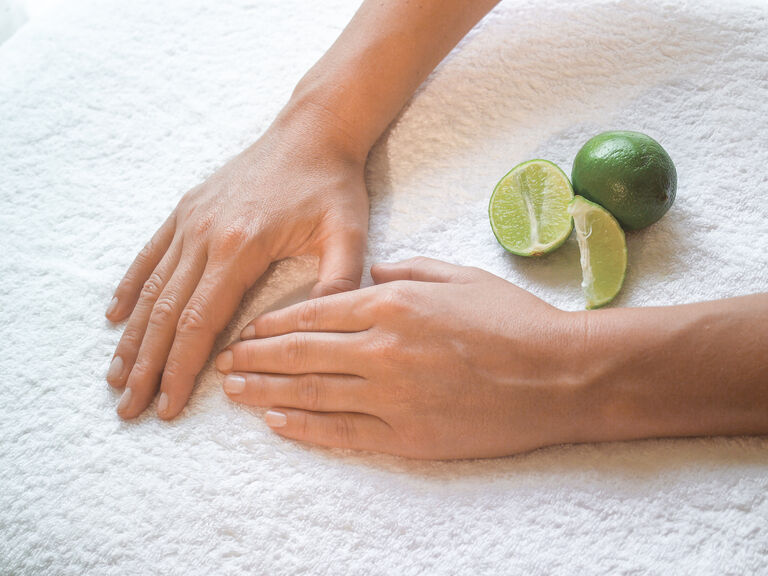 Saubere gepflegte Hände ruhen auf einem Handtuch neben einer frischen Limette.