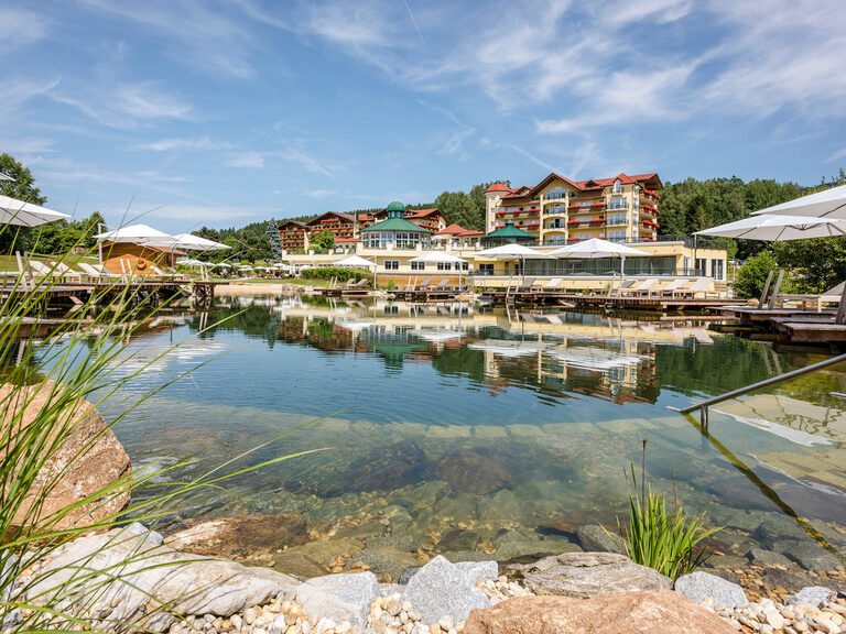 Der Blick auf das traumhafte Wellnesshotel Mooshof mit Naturbadesee, umgeben vom Bayerischen Wald.