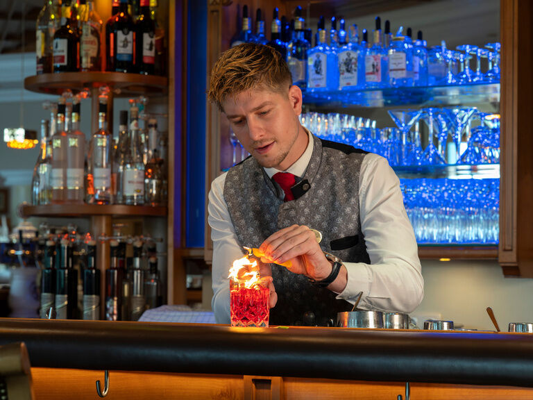 Ein eleganter Barkeeper bereitet einen Cocktail an dem kunstvollen Bartresen zu.
