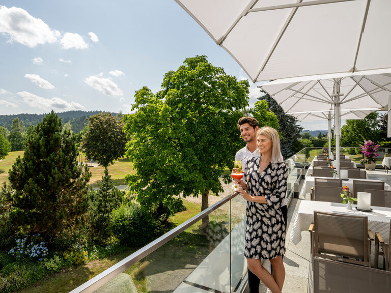 Ein glückliches Paar blickt von der Terrasse des Wellness & SPA Resorts in die Ferne über den Bayerischen Wald.