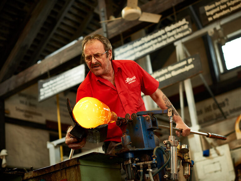 Ein Mann fertigt aus rot glühendem Glas eine Vase.