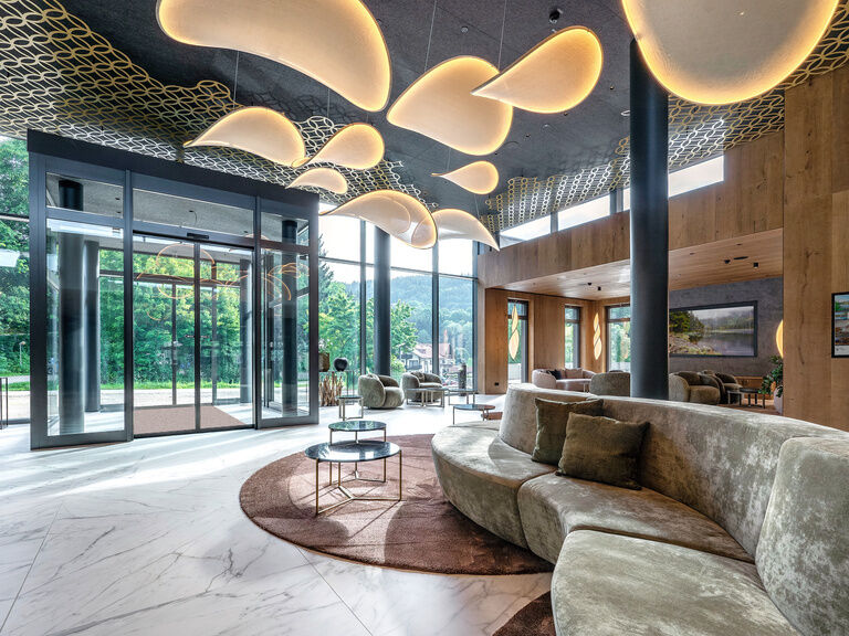 Eine gemütliche Lobby mit Naturmaterialien und großen Glasfenstern im Spa-Hotel Mooshof in Bodenmais.