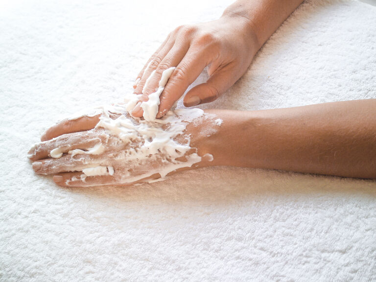 Hände werden auf einem sauberen, weißen Handtuch mit pflegender Handcreme eingecremt.