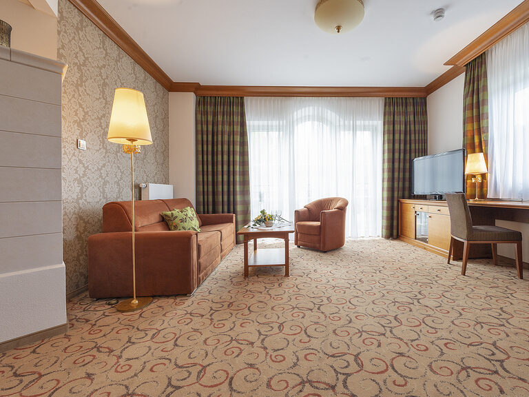 Das geschmackvoll eingerichtete Wohnzimmer in der Hochzell Suite mit gemütlicher Couch und Fernseher im Wellnesshotel Mooshof im Bayerischen Wald.