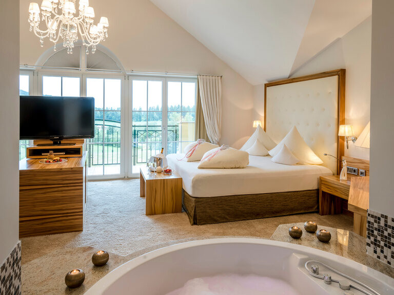 Der große sprudelnde freistehende Whirlpool und ein Bett im luxuriösen Honeymoonsuite-Design des Wellnesshotels Mooshof im Bayerischen Wald.