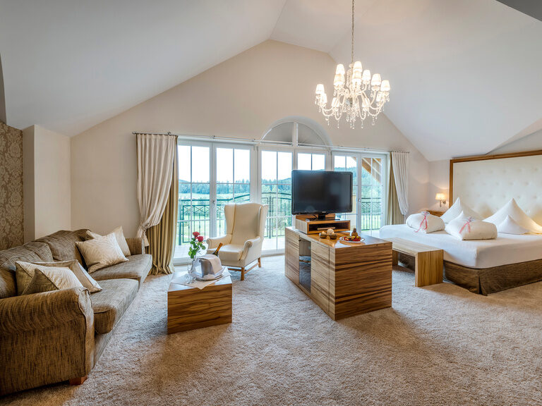 Gemütliche Honeymoon Suite des Wellnesshotels Mooshof in Bayern mit einem komfortablen Bett und Wohnraum direkt vor einem Fenster mit Panoramaausblick.