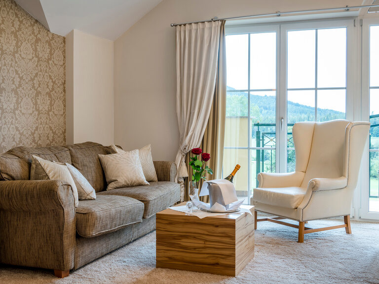 Die geschmackvoll eingerichtete Sitzecke mit hochwertigen Champagner in der Honeymoon-Suite, ergänzt durch kuschelige Wurfkissen lädt zum Entspannen ein..