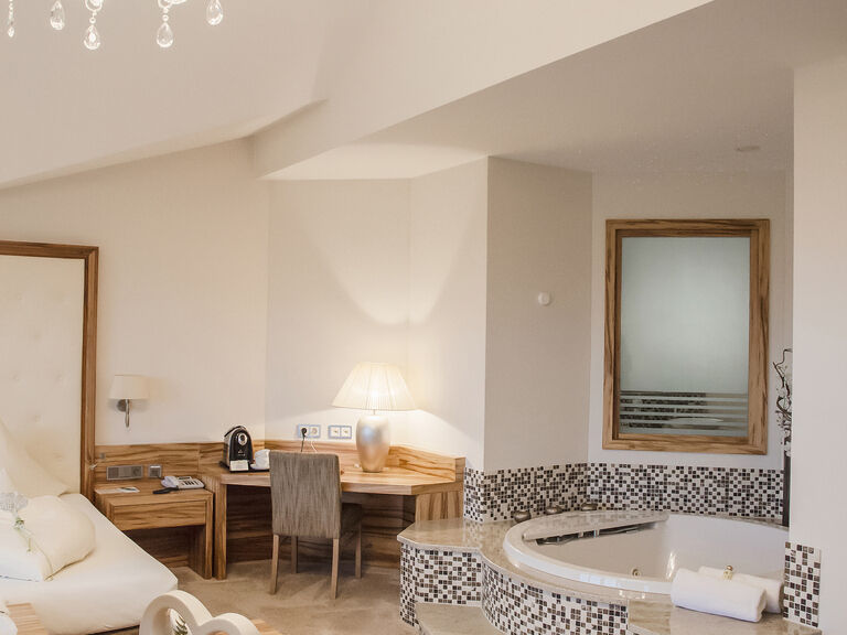 Geschmackvoll eingerichtetes Wohnzimmer in der Honeymoonsuite des Hotels Mooshof in Bayern mit eleganten Möbeln und einem prachtvollen Kronleuchter und freistehender Whirlwanne als Highlight.