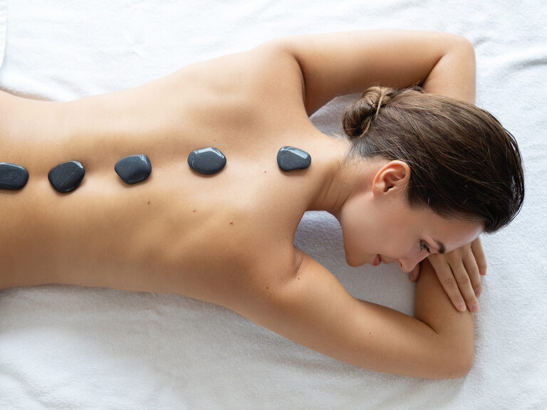 Die sanfte Steinmassage auf dem Rücken einer Frau bietet eine wohltuende Wellnesserfahrung im Wellnesshotel Mooshof im Bayerischen Wald.