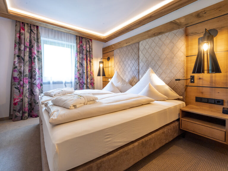 Gemütliches Zimmer Typ 1 mit großen Leuchtelementen im 4-Sterne-Hotel Mooshof in Bayern mit TV und Bett.
