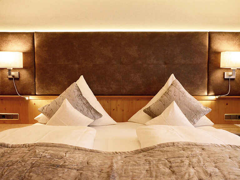 Gemütliches Bett im Hotelzimmer Typ 12 des Wellnesshotels Mooshof in Bayern mit zwei Lampen auf beiden Seiten des Bettes.
