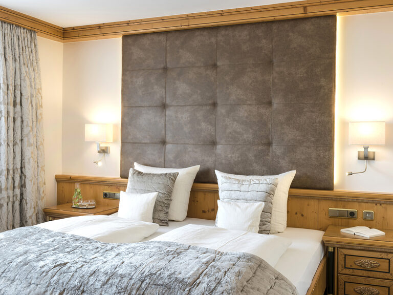 Luxuriöses Schlafzimmer der Landhaussuiten im Wellnesshotel Mooshof in Bodenmais mit modernen Lampen neben einem gemütlichem Bett.