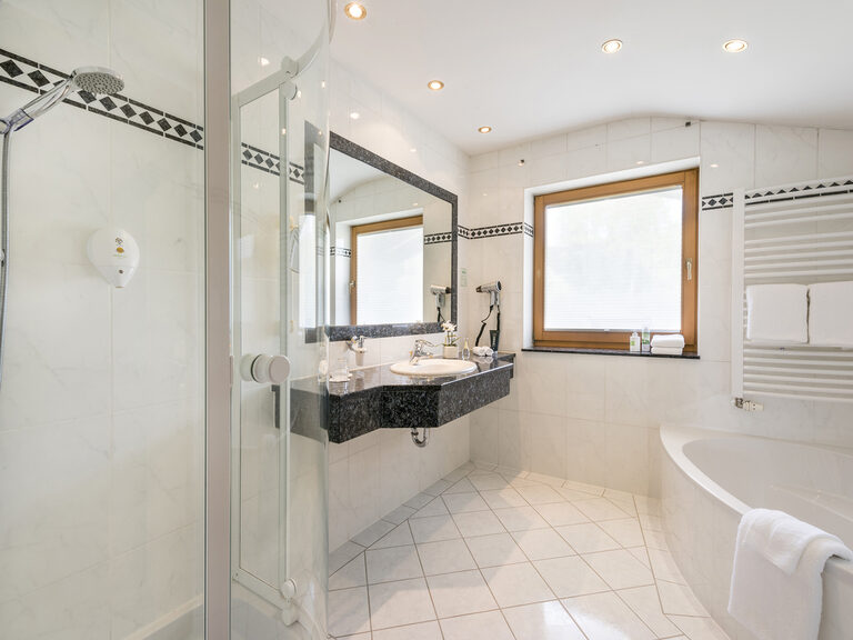 Geschmackvoll eingerichtetes Bad in der Lohwiessuite des Wellnesshotels Mooshof in Bayern, ausgestattet mit großzügigem Spiegel, Dusche und Badewanne.