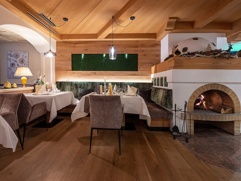 Das elegante Kaminstube Esszimmer mit Tischen und Stühlen lädt zum verweilen vor einem gemütlichen Kamin im Wellnesshotel Mooshof ein.