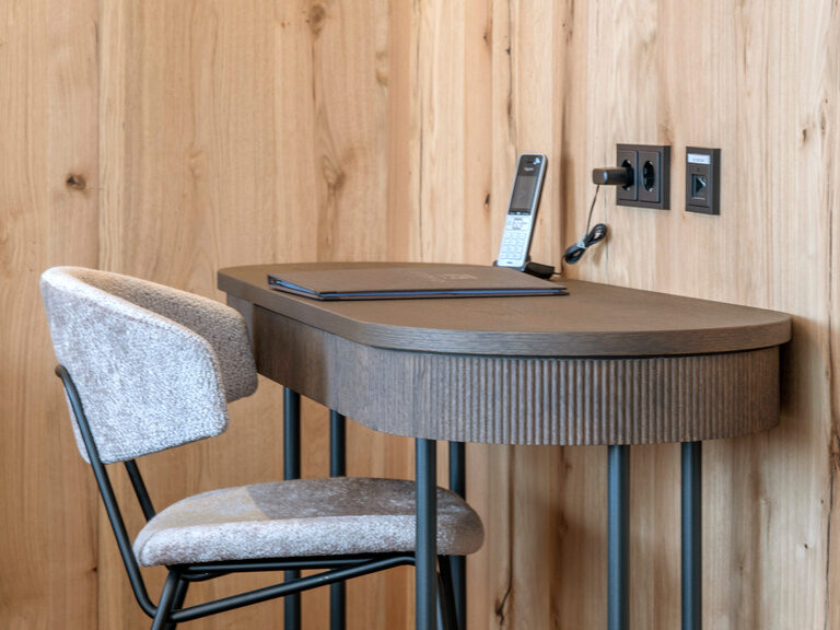 Ein Schreibtisch mit passendem Stuhl auf Parkettboden in Zimmer Typ 3A des Hotels Mooshof im Bayerischen Wald.