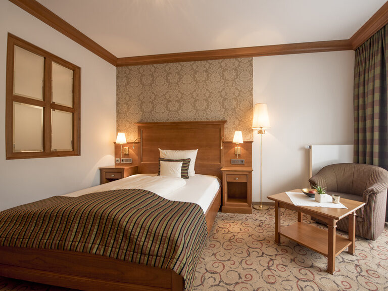 Der elegante Innenraum des Single Suite Hotelzimmers mit einem zentral platzierten Bett und Sessel neben dem Fenster.