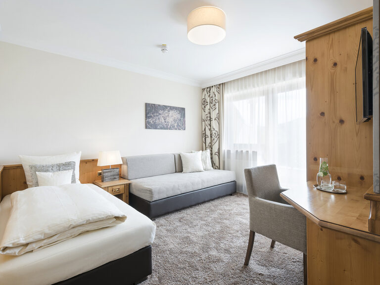 Geschmackvolles Komfortsuite-Zimmer im Hotel Mooshof in Bodenmais mit einem komfortablen Bett und praktischen Arbeitsbereich.