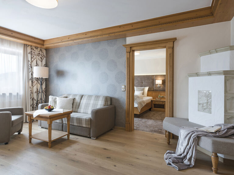 Einladendes Sofa im Wohnbereich der Komfortsuite mit gemütlichem Kachelofen im Wellnesshotel Mooshof im Bayerischen Wald.