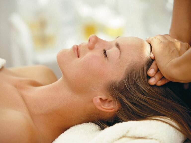 Der Kopf einer Frau wird sanft massiert auf einem Massagetisch im Beauty-Salon des Wellnesshotels Mooshof in Bodenmais.