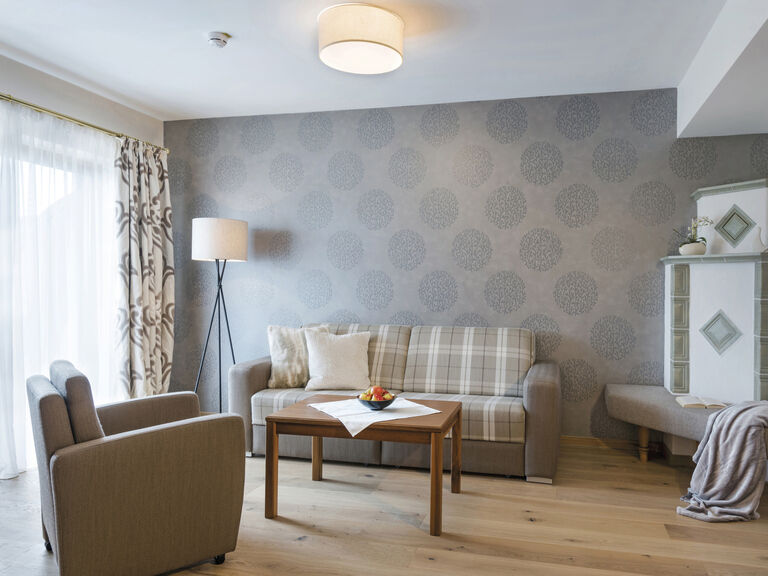 Elegantes Wohnzimmer in den Landhaussuiten des Wellnesshotels Mooshof in Bayern mit hochwertigem Design und einladendem Ambiente durch einen Kachelofen.