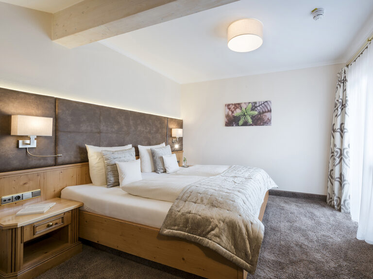 Einladende Möblierung im Schlafbereich der Landhaussuiten im Wellnesshotel Mooshof in Bayern mit warmer Beleuchtung, die Akzente setzt.