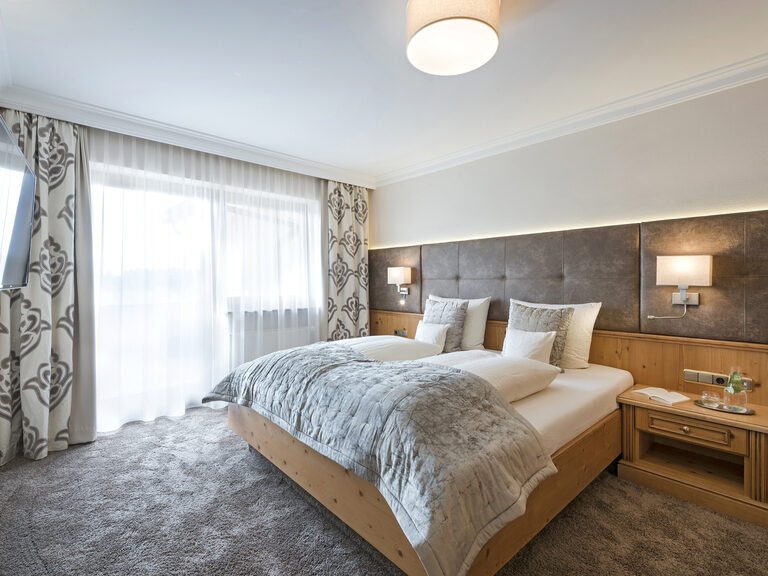 Komfortables Bett und ein moderner Fernseher im geschmackvoll eingerichteten Landhaus Suiten Hotelzimmer des Hotels Mooshof im Bayerischen Wald.