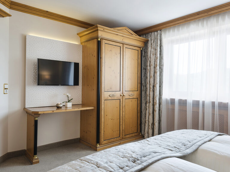 Helles und einladendes Schlafzimmer der Landhaussuiten im Wellnesshotel Mooshof im bayerischen Wald mit einem großen Fenster und einem modernen Fernseher.