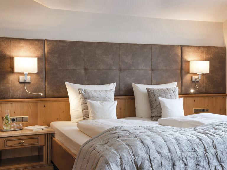 Elegantes Hotelzimmer in der Lohwiessuite des Hotels Mooshof in Bayern mit komfortablem Bett und stimmungsvoller Beleuchtung.