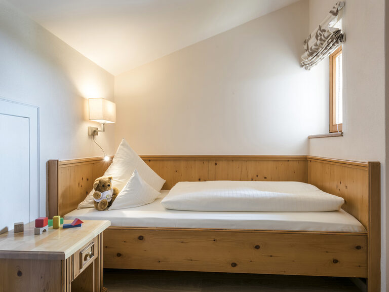 Das Schlafzimmer in der Lohwiessuite im Wellnesshotel Mooshof im Bayerischen Wald bietet ein komfortables Kinderbett und Spielzeug vor schlichten Wänden.