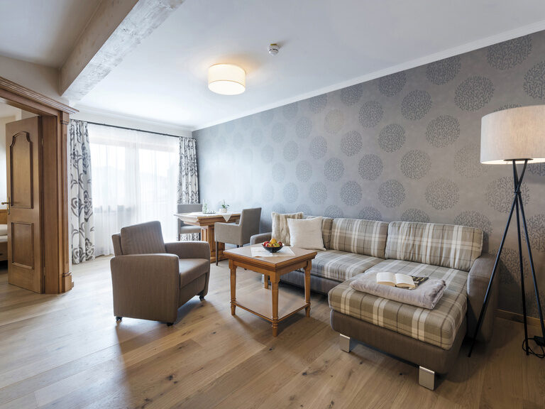 Heller Wohnbereich der Lohwiessuite im Wellnesshotel Mooshof in Bodenmais mit großen Fenstern und stilvollen Möbeln.