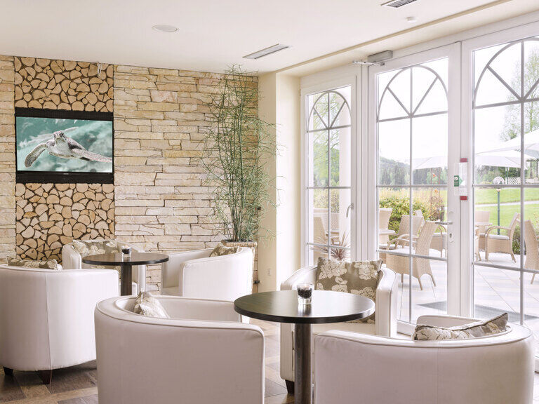 Einladender Loungebereich vor dem großen Terrassenfenster mit gemütlichen runden Sesseln und Fernseher zur Unterhaltung.