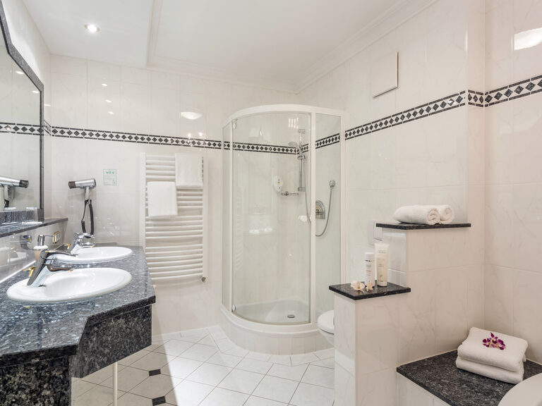 Modernes Badezimmer in der Silberbergsuite des Hotels Mooshof im Bayerischen Wald mit geräumiger Dusche und Waschbecken in markanten, schwarz-weißen Kacheln.
