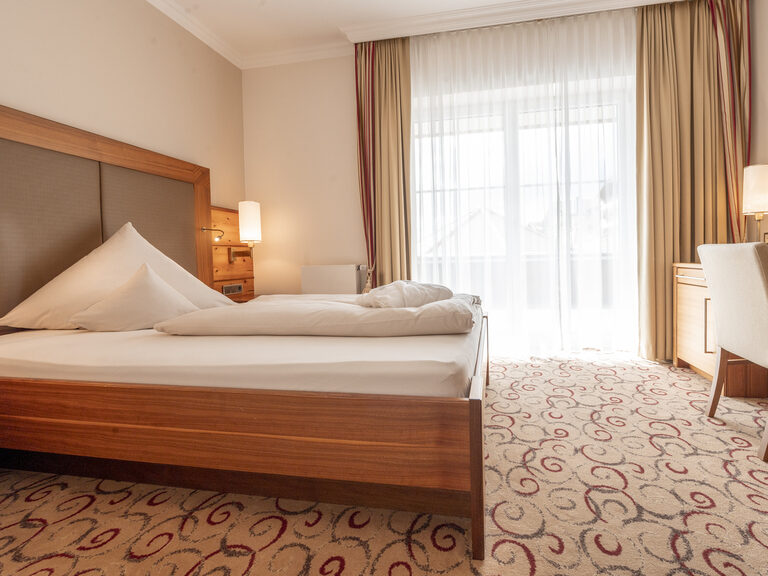 Das charmantes Hotelzimmer des Wellnesshotels Mooshof in Bayern mit einem Schreibtisch, Bett und Fernseher in einem eleganten Design.