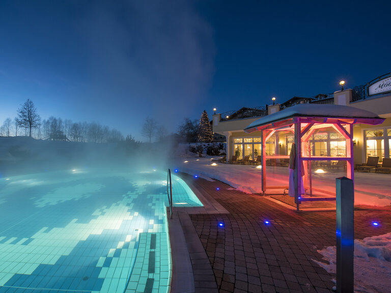 Der Aussenpool im Hotel Mooshof bei Nacht mit Lichtern.