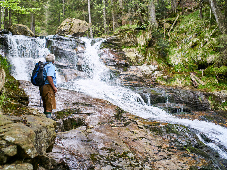 Ein Wanderer steht vor einem rauschenden Wasserfall inmitten der Natur.