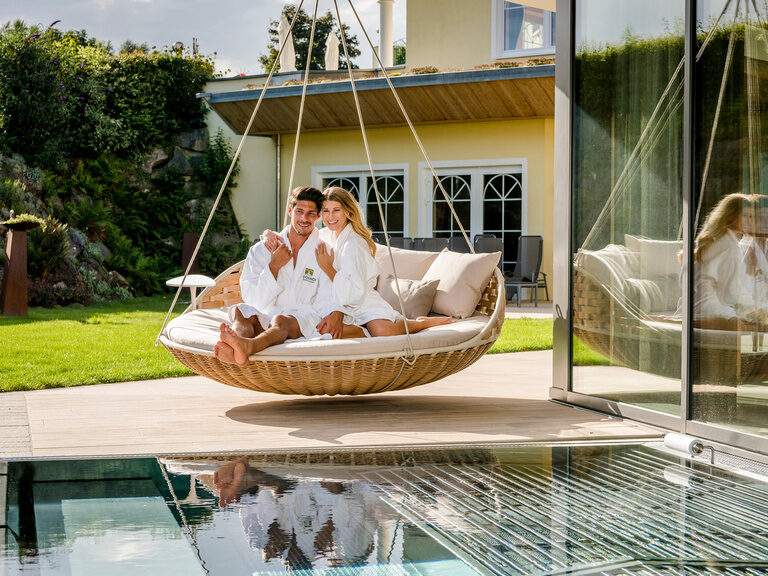 Entspannung pur für ein Paar im Hängesessel nahe dem Schwimmbecken des Wellnesshotels Mooshof in Bodenmais.