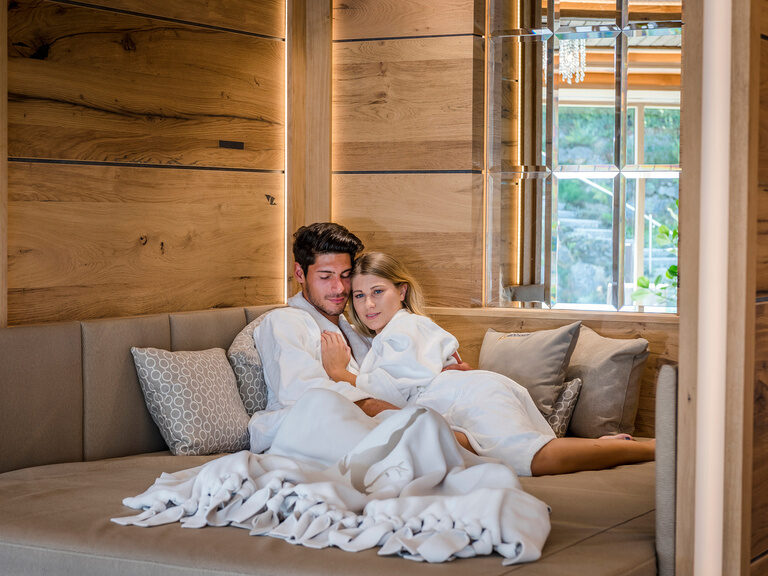 Ein paar entspannt auf einer großen gemütlichen Couch im SPA Bereich des Wellnesshotel Mooshof.