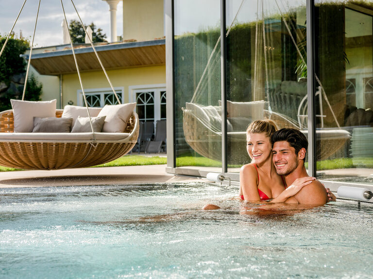 Zwei Personen entspannen im sprudelnden warmen Wasser des Aussenpools im Wellnesshotel Mooshof im Bayerischen Wald.