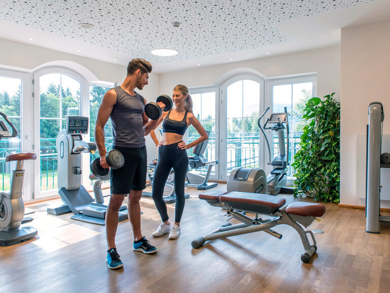 Ein Mann und eine Frau trainieren gemeinsam mit Hanteln im Fitnessraum des Hotels Mooshof im Bayerischen Wald.