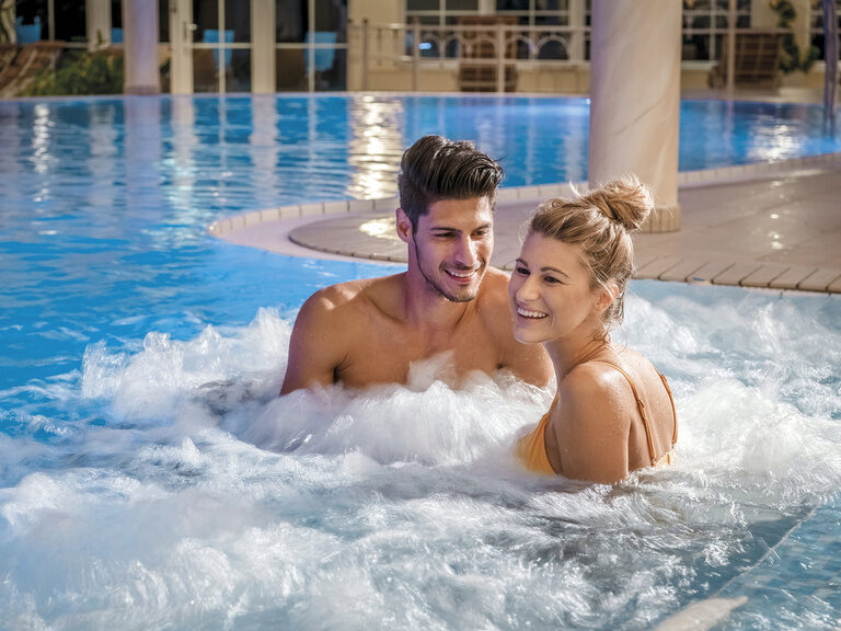 Ein lächelndes Paar genießt die Wellness-Auszeit im Innenpool des Wellnesshotel Mooshof.