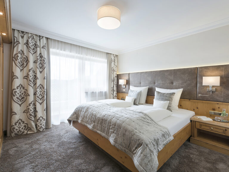 Großes Bett mit gemütlicher Bettwäsche neben dem hellen Südbalkon in der elegant gestalteten Panoramasuite des Hotels Mooshof im Bayerischen Wald.