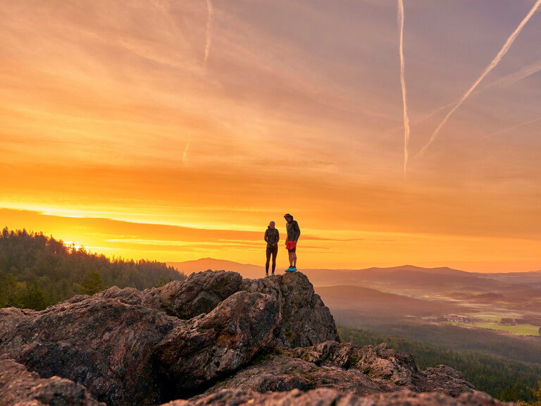 Wanderer genießen den weiten Blick über die Berge bei Dämmerung im Bayerischen Wald.