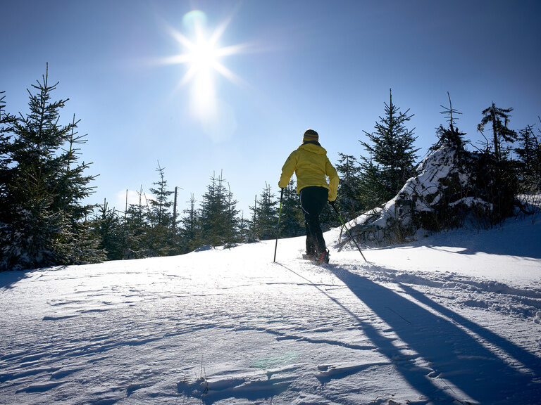 Eine Person beim Wandern auf einem schneebedeckten Hügel in winterlicher Umgebung.