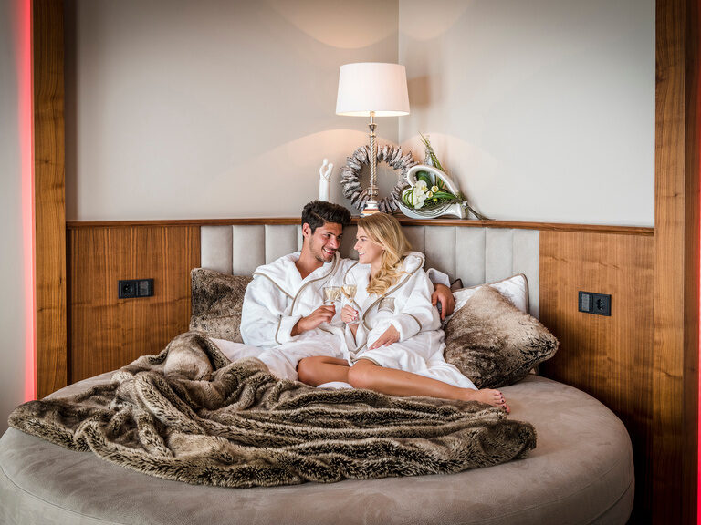 Ein Mann und eine Frau liegen liebevoll auf kuscheligen Bettlaken in der Private Suite des Wellnesshotels Mooshof im Bayerischen Wald.